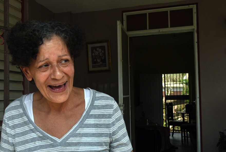 Daly Montavo, born in Puerto Rico and raised in New York City, laughs at her home on Avenida Esteves after filling jugs of water from a National Guard delivery to the neighborhood. She says, "We're here and that's all that matters."