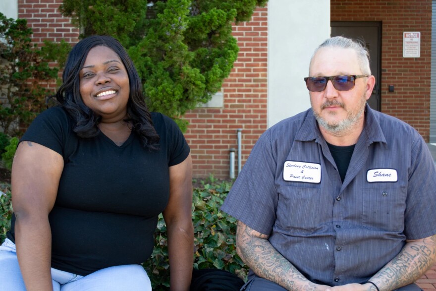 Two people pose for a photo outside of a brick building
