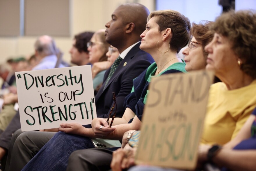 Signs: "Diversity is our STRENGTH" and "Stand With Mason" as people sit and watch the board