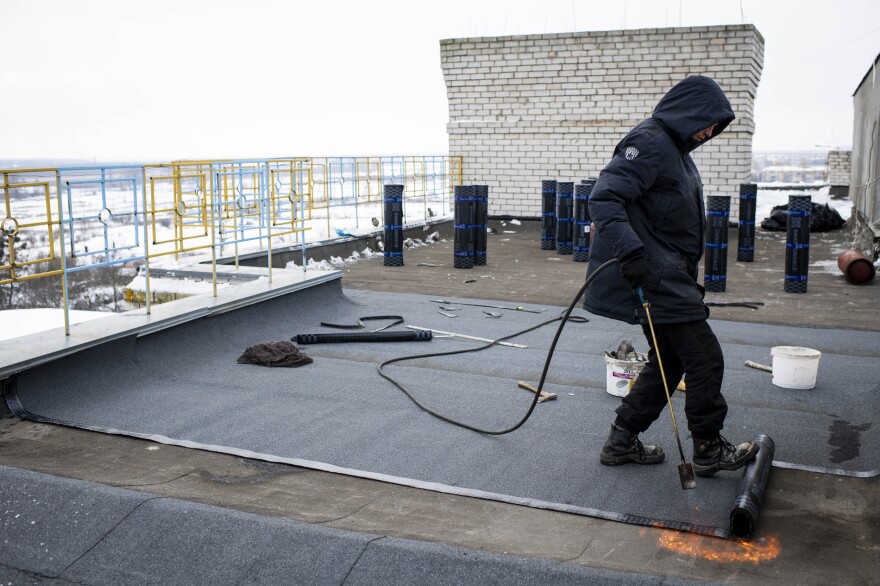Artyom Haydamaka works to repair the roof of a damaged apartment building on the main square in Borodianka on Monday.