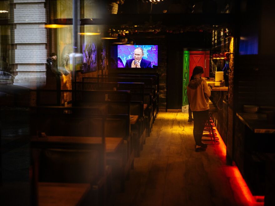 Through a restaurant window, a TV screen shows Russian President Vladimir Putin addressing his annual news conference, in Moscow on Dec. 17, 2020.