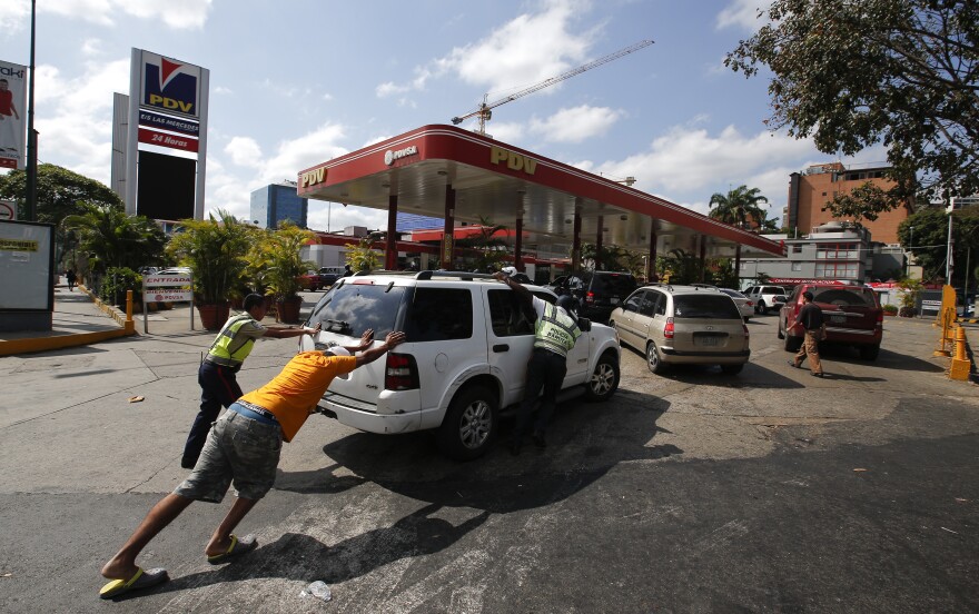 Amid the power outage, people in Caracas push a car without fuel to one of the few gas stations that has its own electric generator.