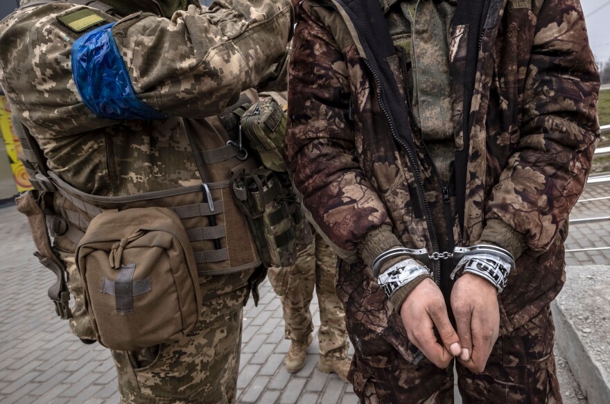 <strong>March 31:</strong> A Ukrainian serviceman stands past a handcuffed Russian soldier in Kharkiv.