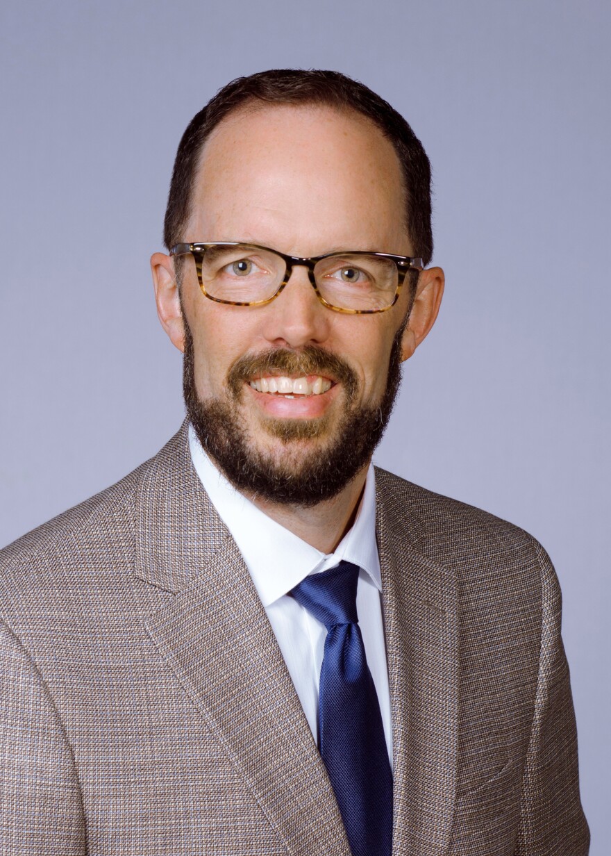 A person in a patterned coat poses for a headshot