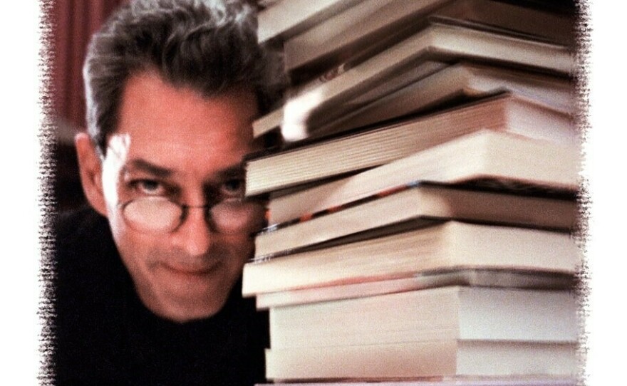 An illustration depicts Paul Auster looking into the camera next to a large stack of books.