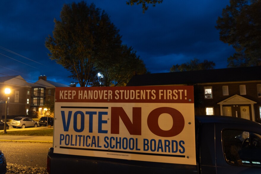 A sign that reads "Keep Hanover students first! Vote NO political school boards" is shown on a vehicle in a neighborhood at night.