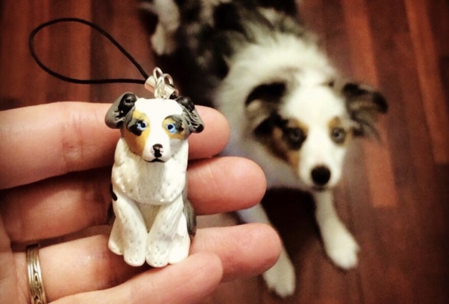 A person holds a dog Christmas ornament in the tips of her fingers, with the dog it was modeled on in the background.