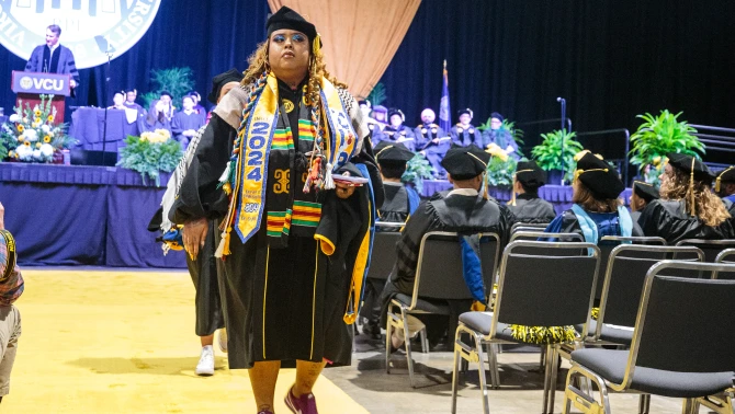 A large group of graduates in black caps and gowns walking out of the Greater Richmond Convention Center during VCU's commencement ceremony.