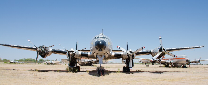 Beneath a cloudless Arizona sky where it is forlornly parked in a sandy field, the first Air Force One is missing parts to its engines. In the shadows beneath its massive wings, scrub brush grows around the wheels of the landing gear. Scattered randomly in the distance behind it, other aircraft from its era languish in the sun.