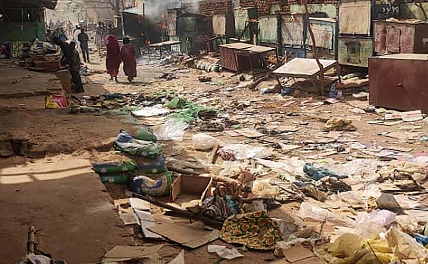 People walk among scattered objects in the market of El Geneina, the capital of West Darfur, as fighting continues in Sudan between the forces of two rival generals, on April 29, 2023.