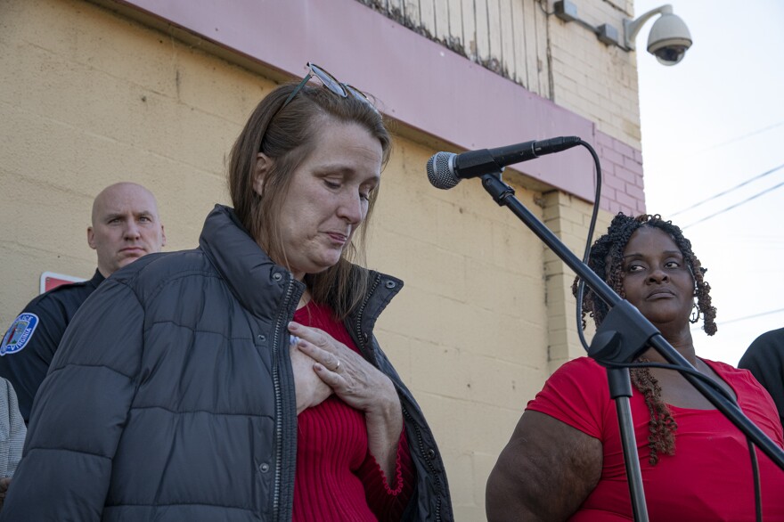 A person with their hands over their heart speaks into a microphone