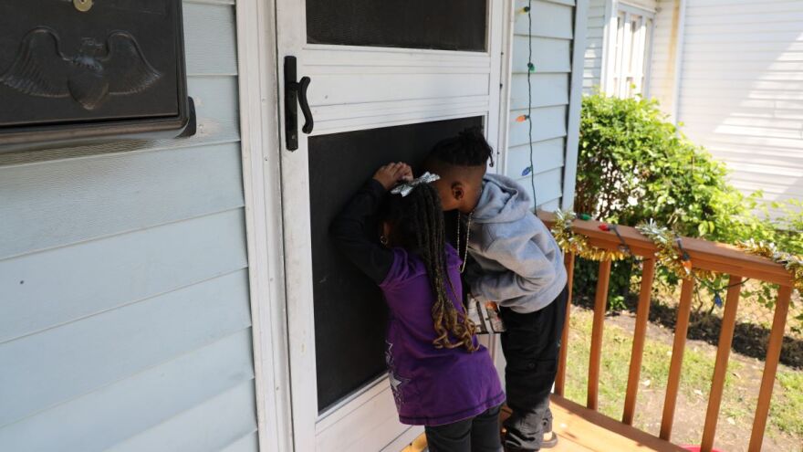 Two young children peak through the a door's screen