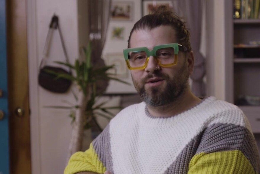 Chest-to-head shot of Scott Tiernan wearing green glasses and a white, gray and yellow sweater.
