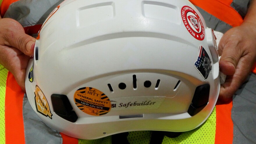 A woman's hands hold a white construction helmet with stickers on it.