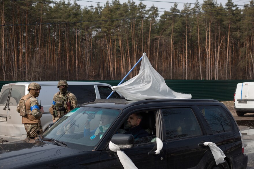 <strong>March 31:</strong> An evacuation car with civilians passes by Ukrainian servicemen in Stoyanka, Ukraine.